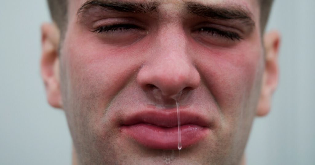 Snot dripping from a man's nose, close-up of facial expression demonstrating congestion and nasal issues.
